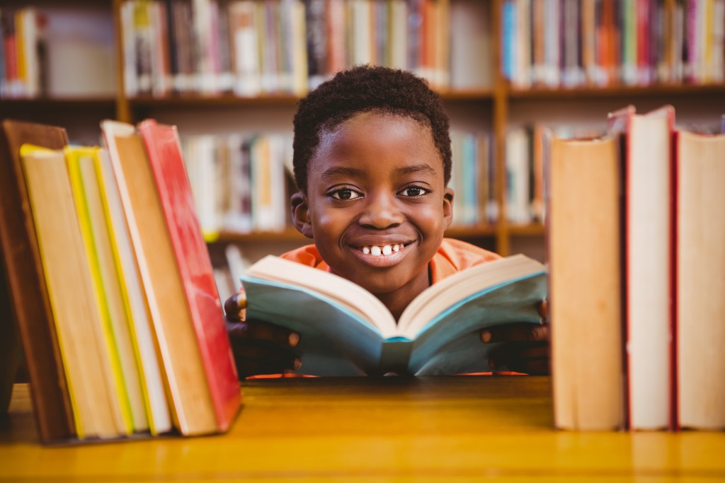 Boy smiling while reading a book in a library.