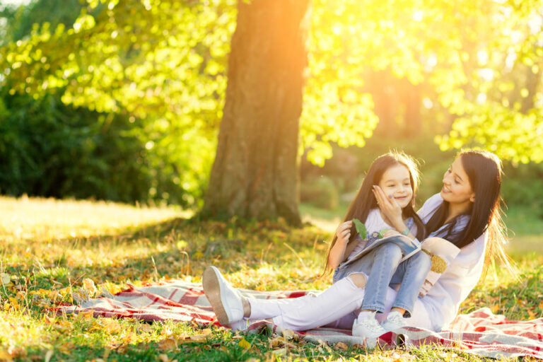 Mother and daughter laughing while reading together in a city park.