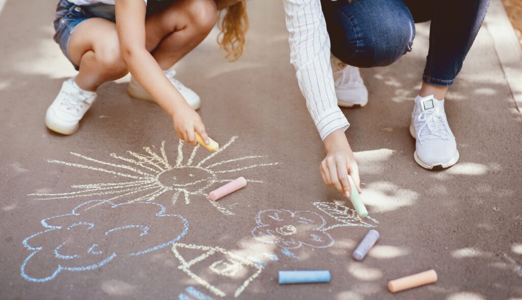 Kids drawing colorful pictures with sidewalk chalk outside.