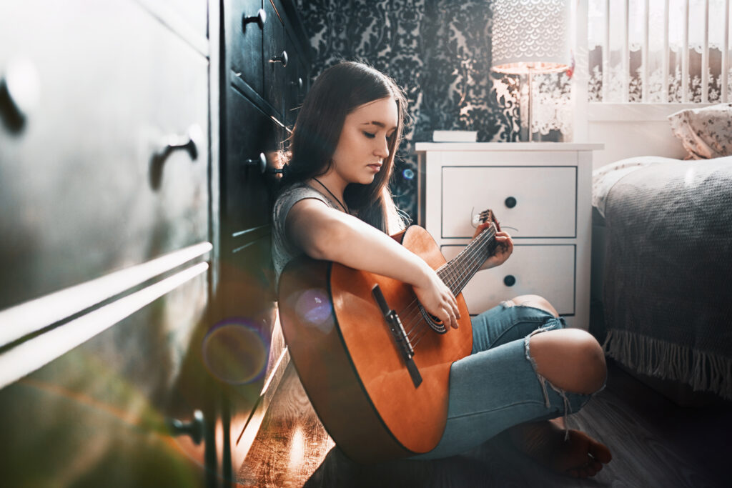 Teen girl playing guitar in her bedroom, showing how music helps children express emotion, creativity, and personal identity