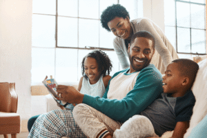 Young father reading SPIDER Magazine with his family at home, showing how analog childhood supports shared reading, focus, and connection