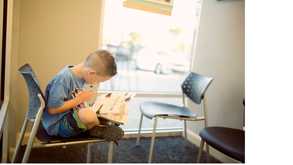 Boy sitting cross-legged in a library chair reading a magazine, showing how analog childhood supports focus, independence, and a love of print