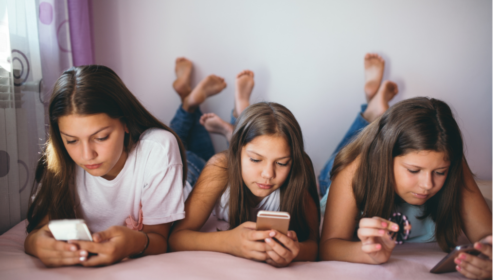 Group of preteen girls lying on a bed and scrolling on smartphones.