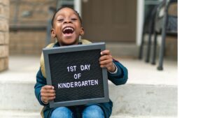 Smiling boy holding a first day of kindergarten sign as his family prepares him for the first day of school.