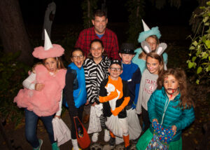 Kids in playful Halloween costumes trick-or-treating with a parent on a not so scary Halloween night